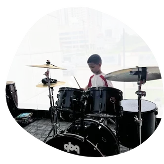 Joven estudiante del Instituto Sol practicando ritmos básicos en la batería durante su clase de percusión, mostrando concentración y entusiasmo